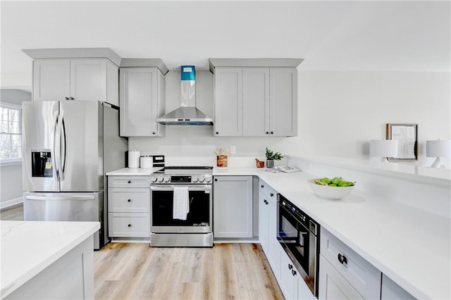 kitchen with wall chimney range hood, light countertops, stainless steel appliances, and light wood-style flooring