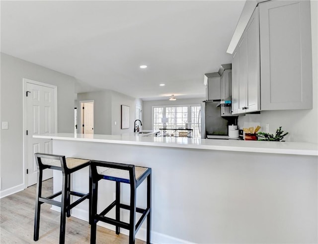 kitchen with freestanding refrigerator, a kitchen bar, light wood-type flooring, recessed lighting, and light countertops