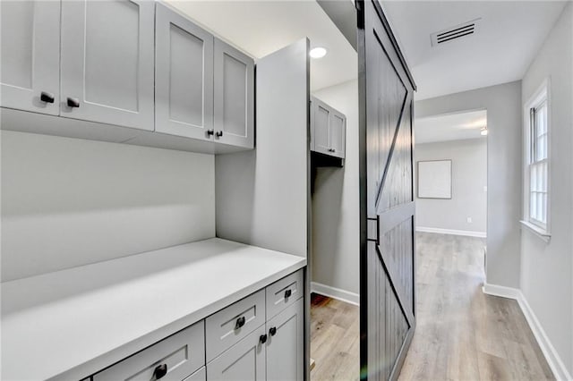 interior space with baseboards, light wood finished floors, a barn door, and visible vents