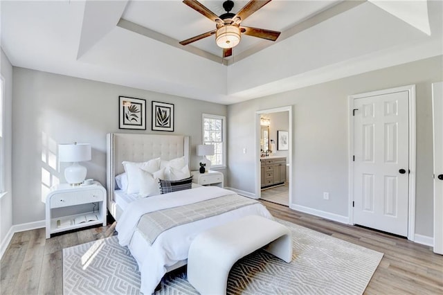 bedroom with a raised ceiling, baseboards, light wood finished floors, and connected bathroom