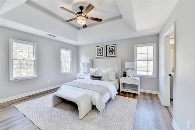 bedroom featuring visible vents, wood finished floors, baseboards, a raised ceiling, and a ceiling fan