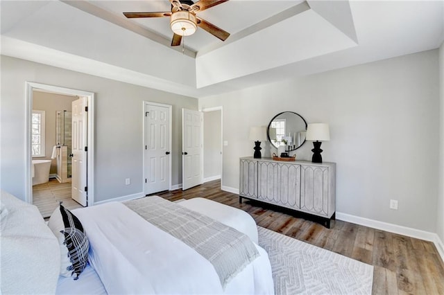 bedroom with a raised ceiling, baseboards, ensuite bath, and wood finished floors