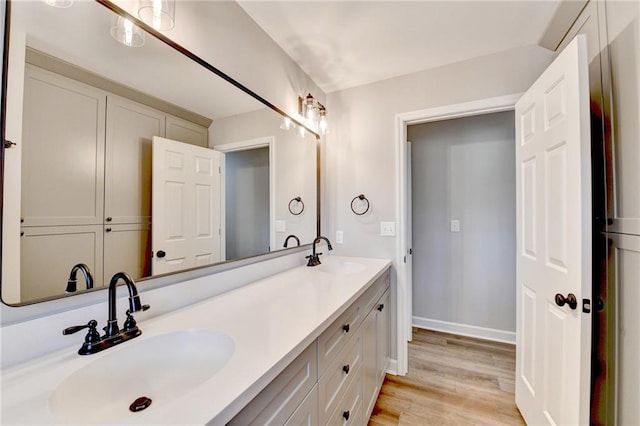 full bathroom featuring a sink, baseboards, double vanity, and wood finished floors