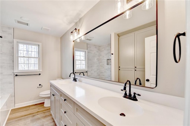 bathroom with a sink, toilet, wood finished floors, and visible vents