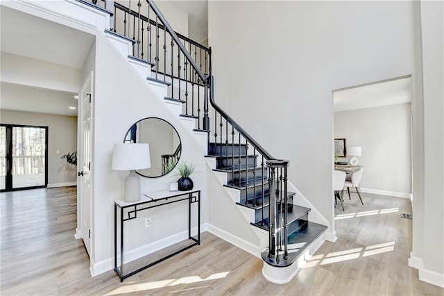 staircase featuring baseboards, a high ceiling, visible vents, and wood finished floors