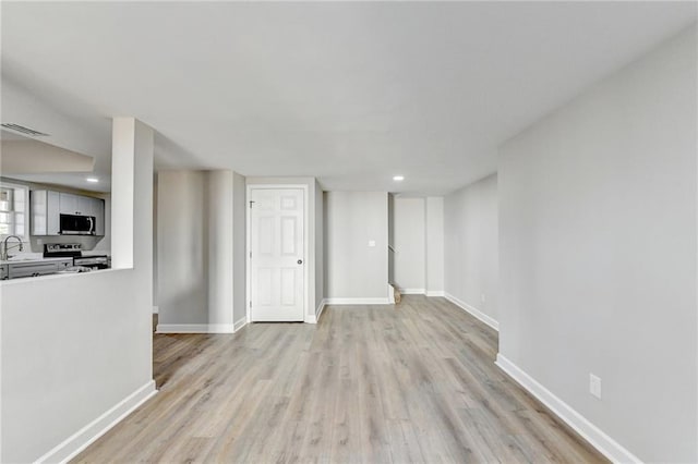 unfurnished living room featuring visible vents, baseboards, recessed lighting, a sink, and light wood-style flooring