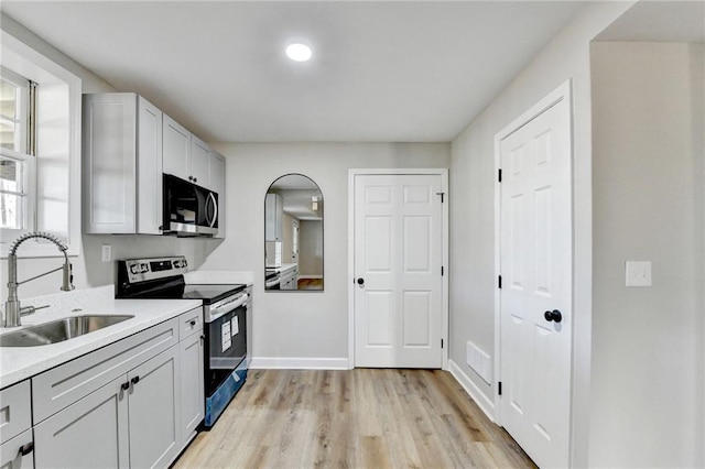 kitchen with light countertops, arched walkways, a sink, light wood-style flooring, and appliances with stainless steel finishes
