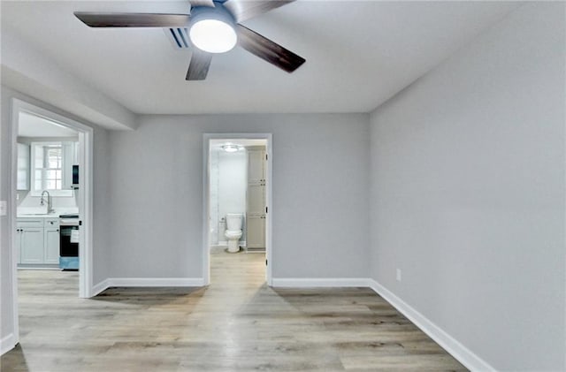 unfurnished room with light wood-type flooring, a sink, baseboards, and ceiling fan