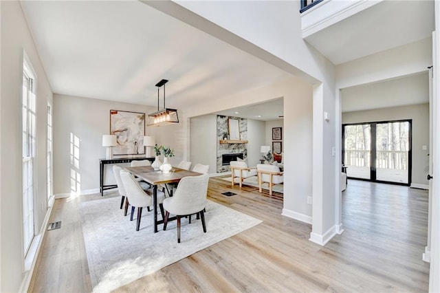 dining area with baseboards, visible vents, a stone fireplace, and light wood-style flooring