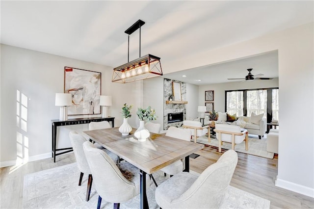 dining room with a large fireplace, baseboards, a ceiling fan, and light wood-style flooring