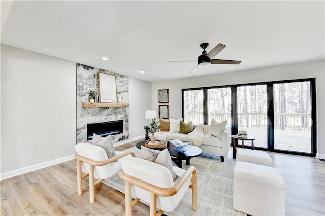 living room featuring baseboards, ceiling fan, a large fireplace, and light wood-style flooring
