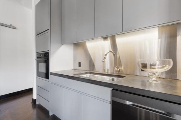 kitchen with a sink, dishwasher, dark wood finished floors, modern cabinets, and black oven