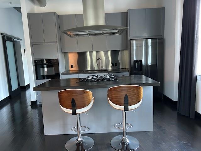 kitchen with island exhaust hood, modern cabinets, dark countertops, appliances with stainless steel finishes, and gray cabinets