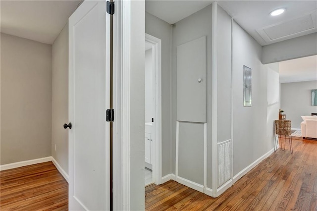 hall with light wood-style flooring, visible vents, baseboards, electric panel, and attic access