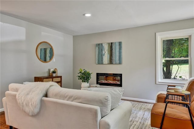 living room featuring recessed lighting, a glass covered fireplace, and baseboards