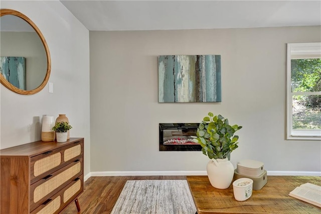 sitting room featuring dark wood-style flooring, a glass covered fireplace, and baseboards