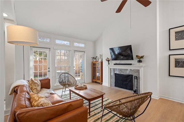 living area with light wood-type flooring, ceiling fan, baseboards, and a high end fireplace