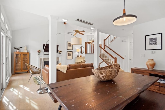 dining room featuring lofted ceiling, a tile fireplace, visible vents, stairs, and light wood finished floors