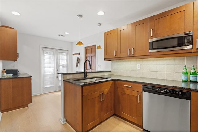 kitchen with hanging light fixtures, appliances with stainless steel finishes, brown cabinetry, a sink, and a peninsula