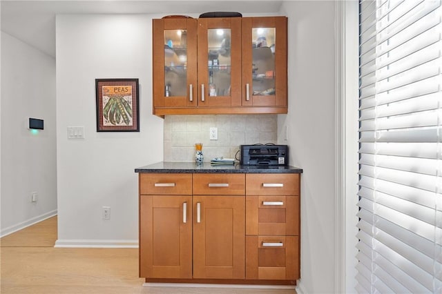 kitchen featuring baseboards, decorative backsplash, glass insert cabinets, brown cabinets, and light wood-style floors