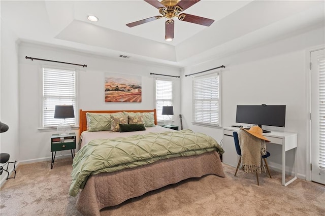 bedroom featuring ceiling fan, light carpet, visible vents, baseboards, and a raised ceiling