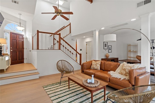 living room featuring visible vents, decorative columns, stairway, and light wood finished floors