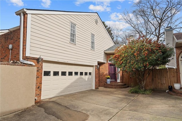 view of side of property featuring a garage, fence, concrete driveway, and brick siding