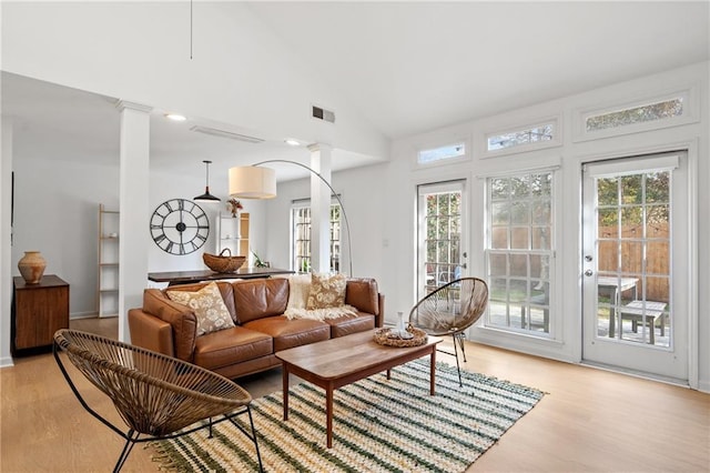 living area with high vaulted ceiling, ornate columns, visible vents, and light wood finished floors