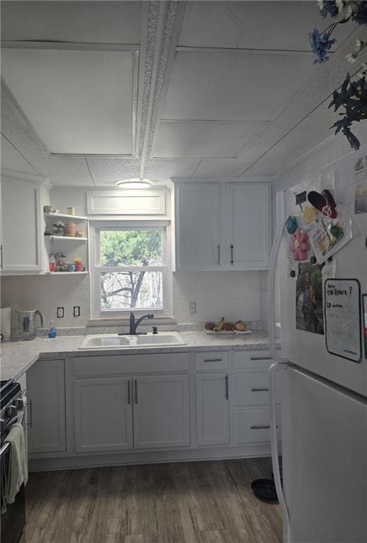 kitchen with dark wood finished floors, freestanding refrigerator, white cabinetry, a sink, and gas range