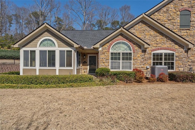 ranch-style house featuring stone siding, central air condition unit, and a shingled roof