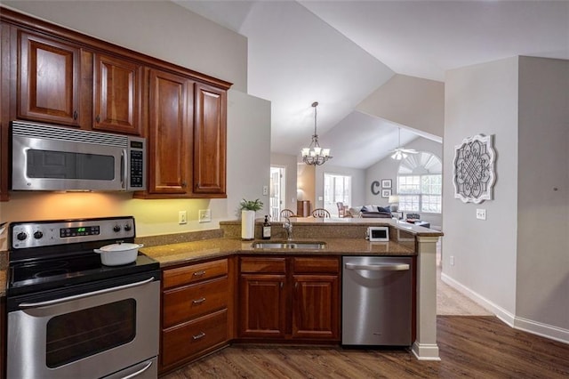 kitchen featuring open floor plan, dark stone counters, appliances with stainless steel finishes, a peninsula, and a sink