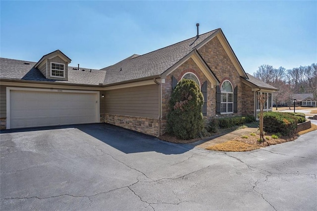 ranch-style home with aphalt driveway, a garage, stone siding, and roof with shingles