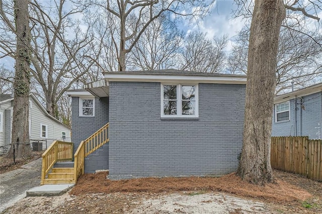 view of front of property featuring cooling unit, brick siding, and fence