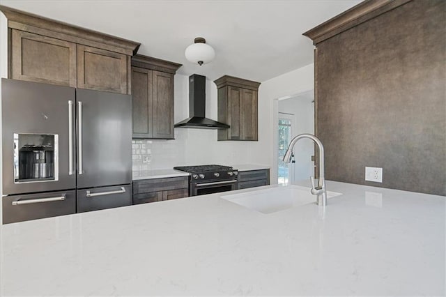 kitchen featuring wall chimney range hood, dark brown cabinetry, high quality appliances, decorative backsplash, and a sink