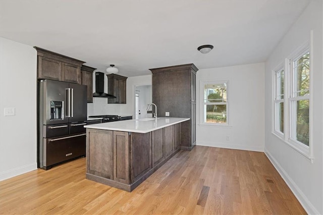 kitchen featuring dark brown cabinets, light countertops, black appliances, wall chimney exhaust hood, and a sink