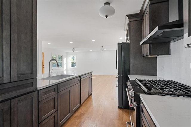 kitchen featuring light wood-style flooring, a sink, stainless steel appliances, dark brown cabinetry, and wall chimney exhaust hood