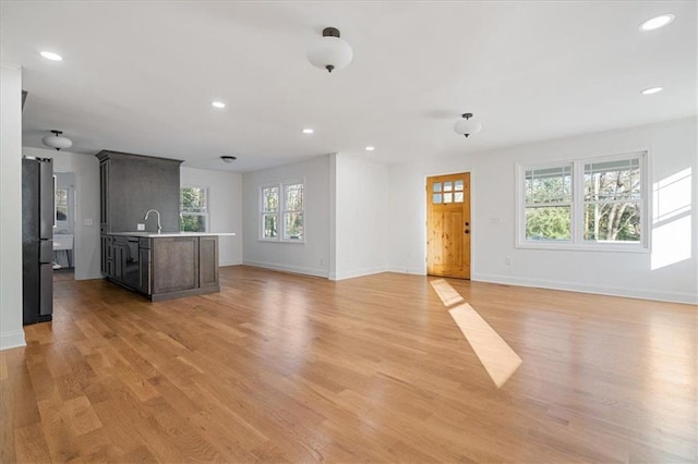 unfurnished living room featuring recessed lighting, baseboards, light wood-style floors, and a sink