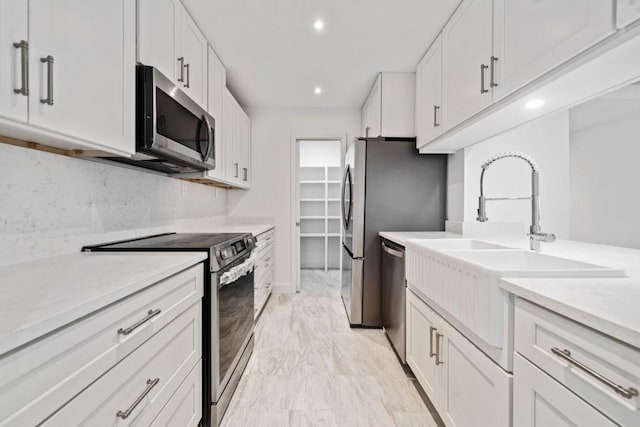 kitchen featuring recessed lighting, a sink, stainless steel appliances, white cabinets, and tasteful backsplash