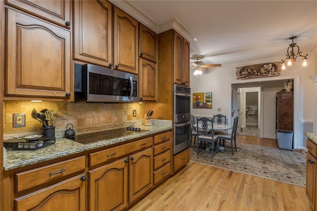 kitchen with pendant lighting, light hardwood / wood-style floors, light stone countertops, ceiling fan with notable chandelier, and appliances with stainless steel finishes