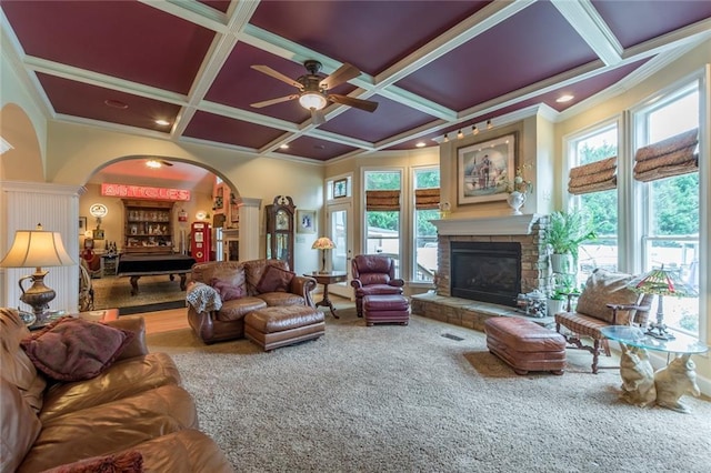 living room featuring coffered ceiling, a healthy amount of sunlight, a stone fireplace, and crown molding