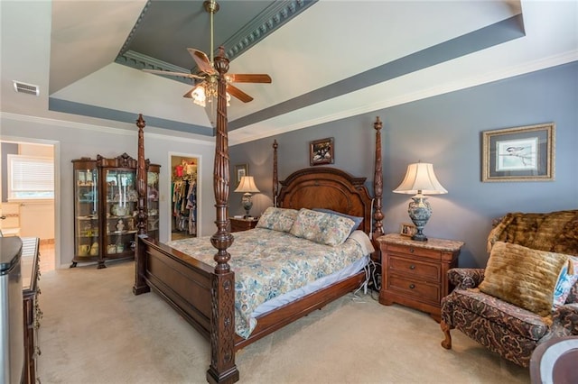 bedroom featuring light colored carpet, ceiling fan, a walk in closet, a tray ceiling, and a closet