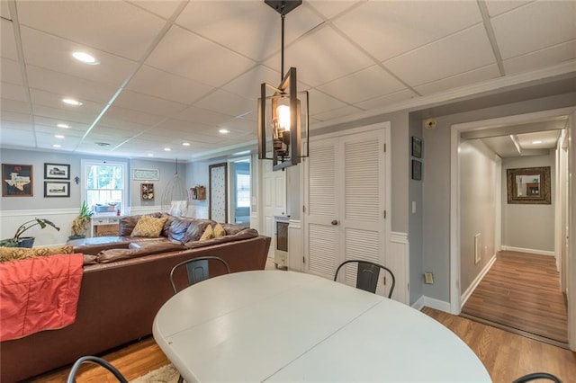 dining area with light hardwood / wood-style floors, a drop ceiling, and ornamental molding