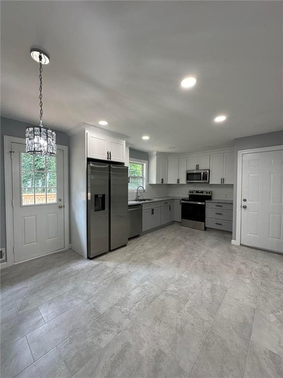 kitchen featuring white cabinetry, sink, hanging light fixtures, an inviting chandelier, and appliances with stainless steel finishes