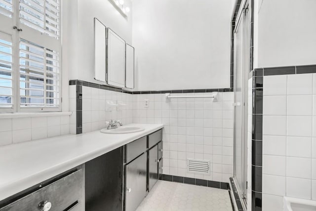 bathroom with vanity, a shower with shower door, and tile walls