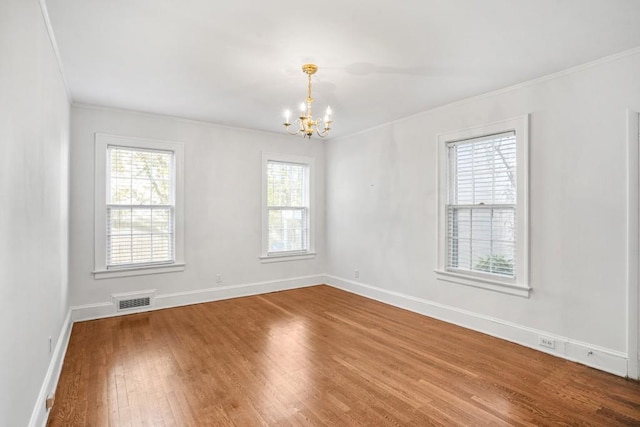 spare room with a chandelier, hardwood / wood-style floors, and crown molding