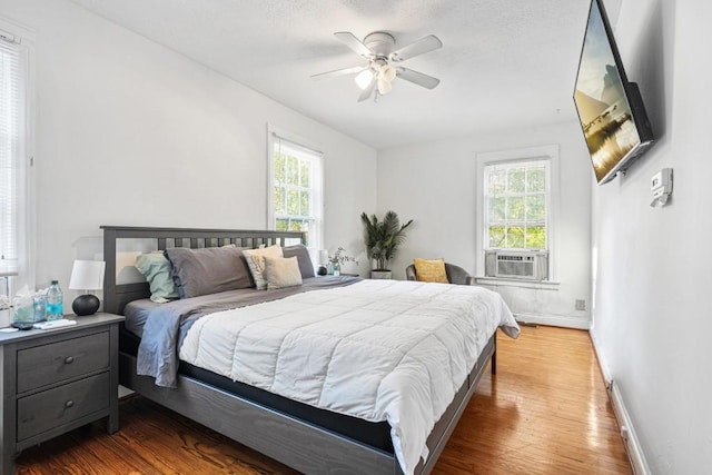 bedroom with hardwood / wood-style flooring, multiple windows, cooling unit, and ceiling fan