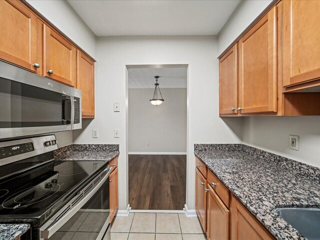 kitchen featuring dark stone countertops, hanging light fixtures, light tile patterned floors, and stainless steel appliances