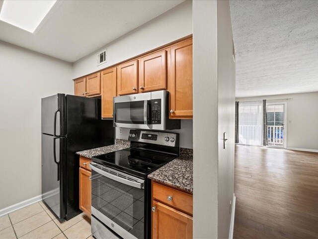 kitchen with dark stone counters, a textured ceiling, appliances with stainless steel finishes, and light hardwood / wood-style flooring