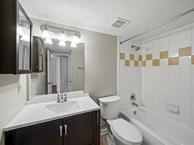 full bathroom featuring tiled shower / bath, vanity, a textured ceiling, and toilet