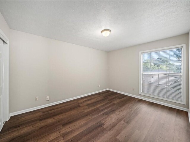 empty room with a textured ceiling and dark wood-type flooring